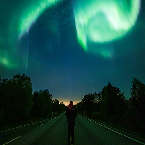 Nordlichter über Person auf Straße © Apukka Resort