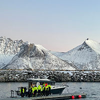 Boot mit Personen im Wasser vor verschneitem Berg in Norwegen © Best Arctic